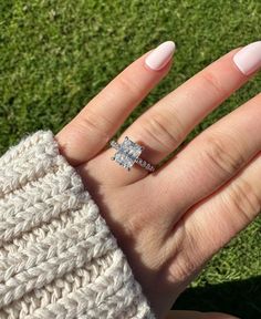 a woman's hand with a ring on top of her finger, in the grass