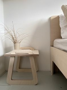 a small wooden table sitting next to a bed in a room with white walls and flooring