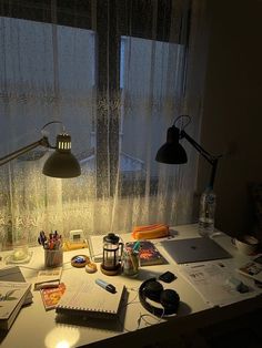 a desk with a lamp, notebooks and other items on it next to a window