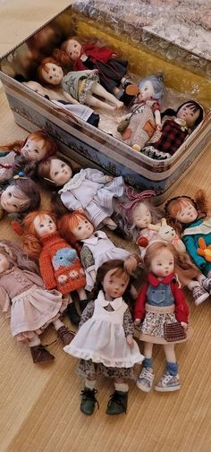 a bunch of dolls that are sitting on the floor next to a tin box full of them