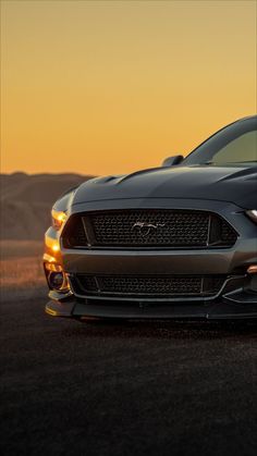 the front end of a black mustang parked in an open field at sunset with mountains in the background