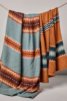 an orange and blue blanket hanging on a clothes line with two pieces of cloth draped over it