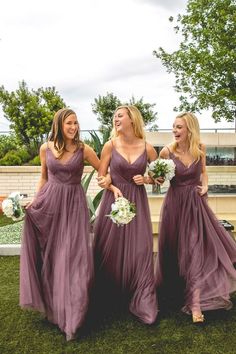 three bridesmaids in long purple dresses laughing at each other on the grass outside