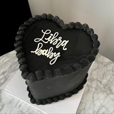 a black heart shaped cake sitting on top of a white marble table with the words happy birthday written on it