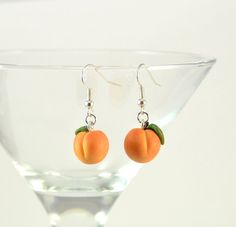 two small oranges are hanging from silver earwires on a martini glass rim