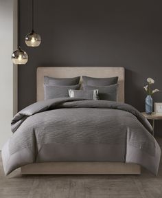 a bed with grey comforter and pillows in a gray room next to two lamps