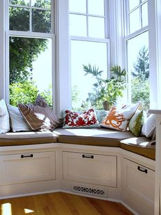 a corner window seat with lots of pillows on it in front of a wooden floor