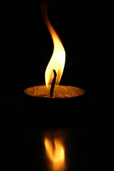 a candle that is lit in the dark with some light coming from it and its reflection on the ground