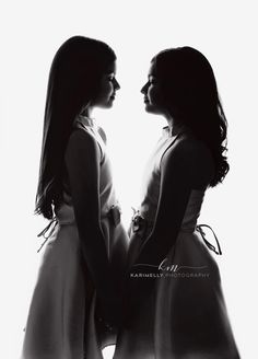 two women standing next to each other in front of a white background and looking at each other