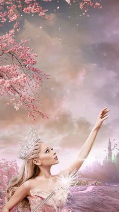 a beautiful woman in a white dress and tiara standing under a tree with pink flowers