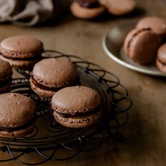 chocolate macaroons sitting on a wire rack next to other cookies and pastries