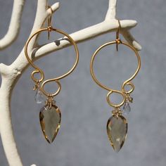 a pair of gold hoop earrings with green and clear crystal stones hanging from them on a branch