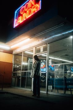 a man standing in front of a neon sign on the side of a building at night