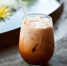 an iced drink in a glass with a straw sitting on a table next to flowers