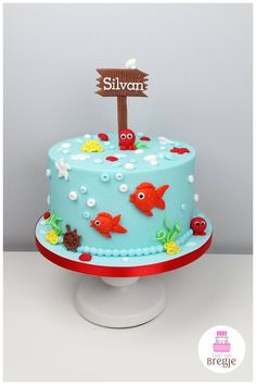 there is a blue cake with fish on it and a wooden sign that says,