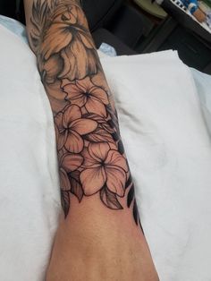 a woman's arm with flowers on it in black and grey ink, sitting on a bed