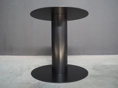 a black round table sitting on top of a white floor next to a gray wall