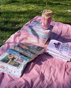 a pink blanket sitting on top of a lush green field next to a pile of books