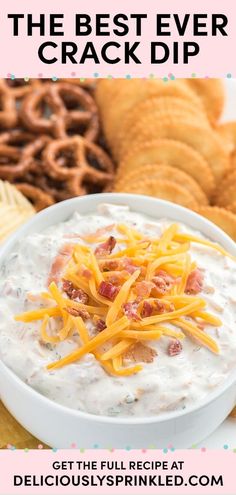 a white bowl filled with dip surrounded by crackers and pretzels