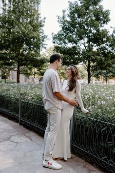 a man and woman standing next to each other near a fence with flowers in the background