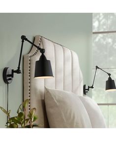 a bed with two lamps on the headboard and one light is turned on in front of a window