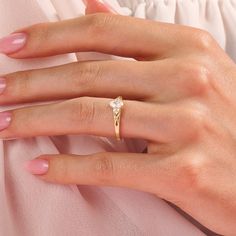 a woman's hand wearing a gold ring with a diamond on the middle finger