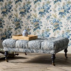 an upholstered bench in front of a floral wallpaper