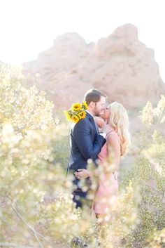 a couple kissing in the desert with sunflowers on their forehead and mountains behind them