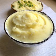 a bowl filled with mashed potatoes sitting on top of a white table next to bread