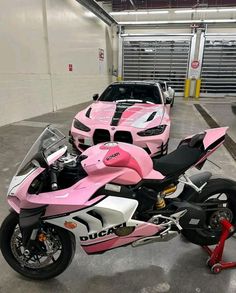 a pink motorcycle parked next to a white car in a parking garage with other vehicles