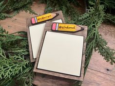 two notepads sitting next to each other on top of a wooden table with pine branches