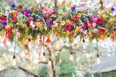 an arrangement of flowers hanging from a tree with light bulbs and lightshades in the background