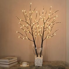 a vase filled with branches and lights on top of a fur covered table next to a book