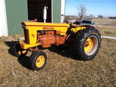 an old yellow tractor parked in front of a barn