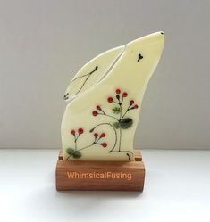 two white ceramic birds with red berries on them sitting on a wooden stand in front of a gray wall