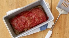 a meatloaf in a pan with a spatula next to it on a wooden table