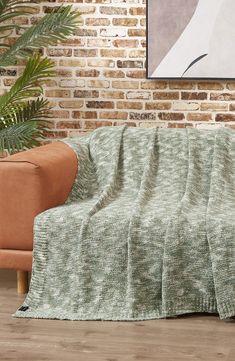 a couch with a blanket on it in front of a brick wall and potted plant