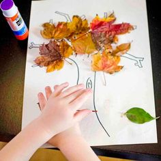 a child's hand is on the paper with leaves