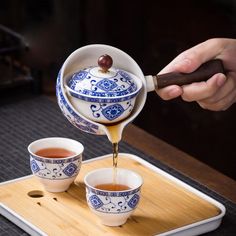 a person pours tea into two cups on a tray with chopsticks and saucer