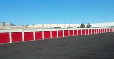 a row of storage units with red doors on each side and one empty parking lot behind them