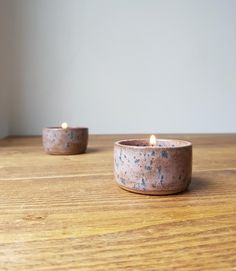 two candles sitting on top of a wooden table next to each other, one lit