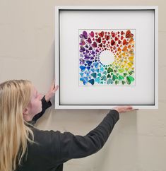 a woman is holding up a framed art piece with butterflies in rainbow colors on it