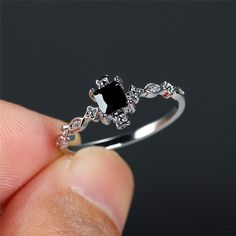 a person is holding a ring with a black stone in the middle and white diamonds around it