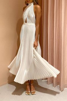 a woman standing in front of a window wearing a white dress with pleated skirt