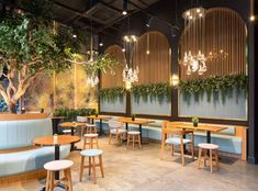 an empty restaurant with blue booths and wooden tables in front of plants on the wall