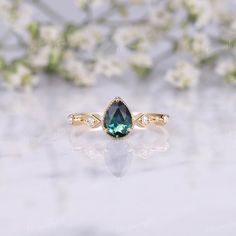 a ring with a green stone in the middle and white flowers behind it on a table