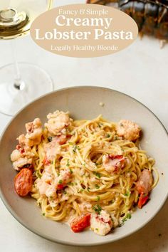 creamy lobster pasta in a white bowl with a glass of wine on the side