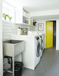 a washer sitting next to a sink in a room with tiled floors and walls