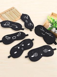 five black sleeping masks with faces drawn on them, sitting on a table next to a plant