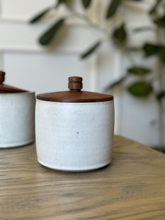 two white ceramic containers sitting on top of a wooden table